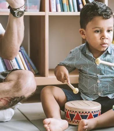 Toddler with a toy drum with a parent sitting next to him